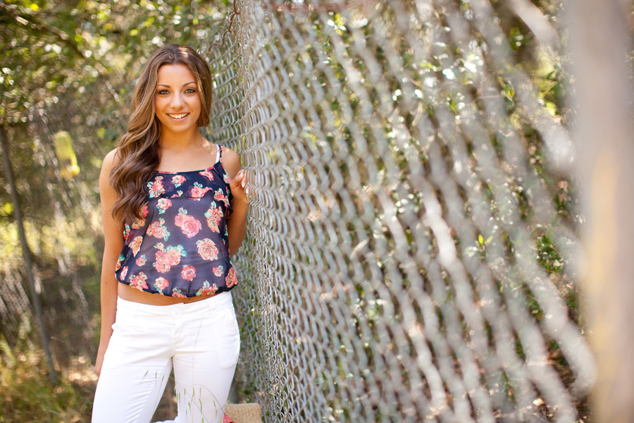 Kristina leans up on a fence and smiles for her senior year at Gilroy High.