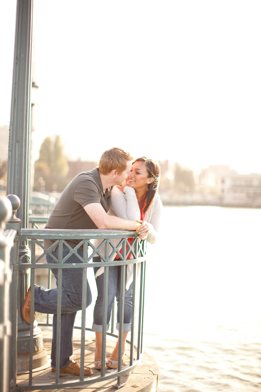The couple lean on the pier railing looking at each other.