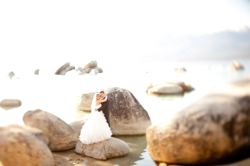 The bride and groom stand on a rock in the middle of Lake Tahoe.