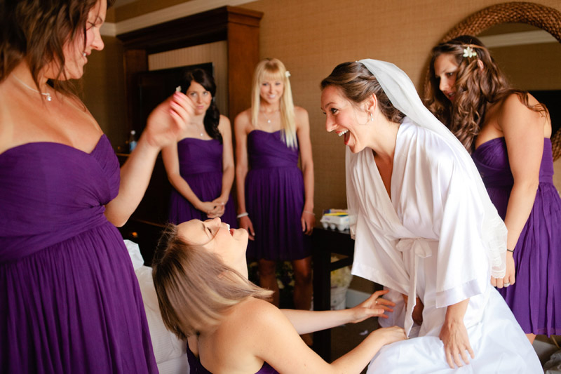 Brittany and her bridesmaids laugh while she puts her wedding dress on.