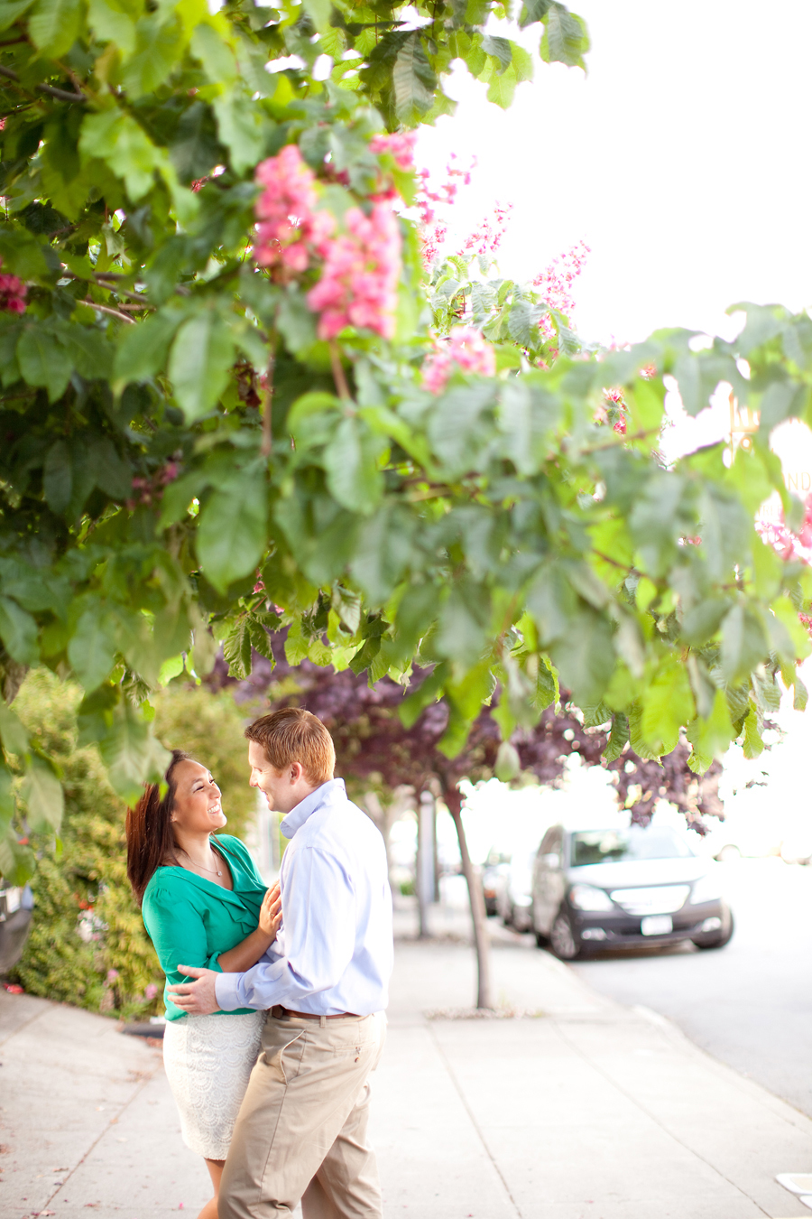 The couple stands on the San Francisco sidewalk under a tree.